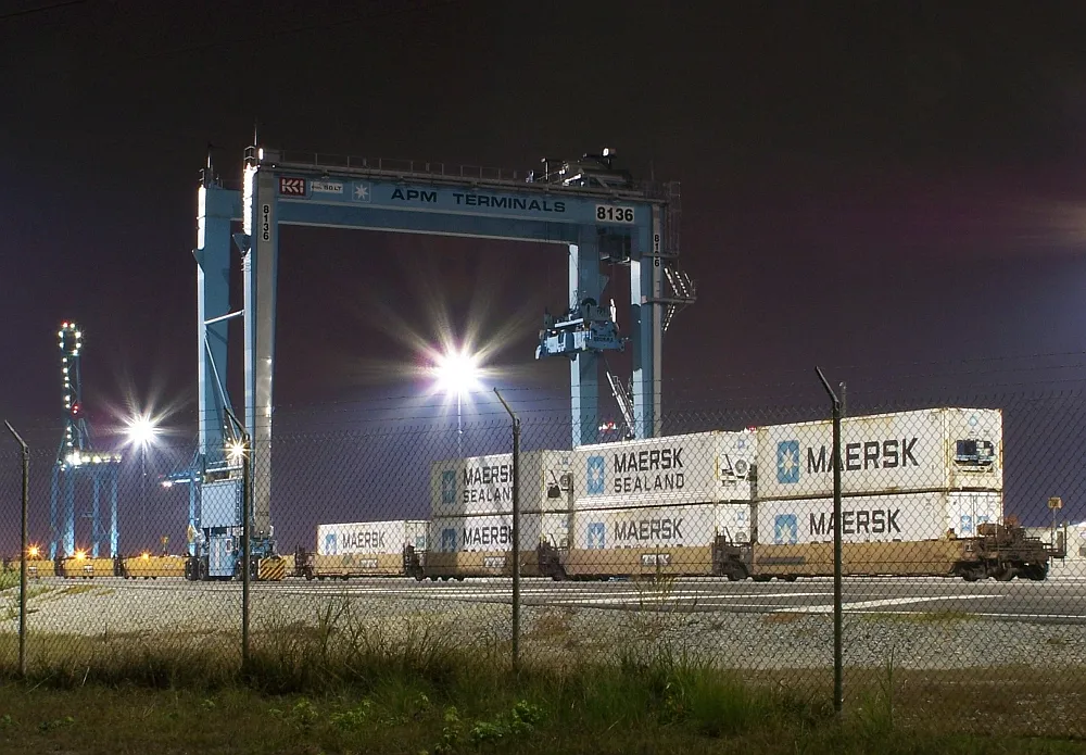 Maersk containers stacked under a gantry crane at an APM Terminals yard at night